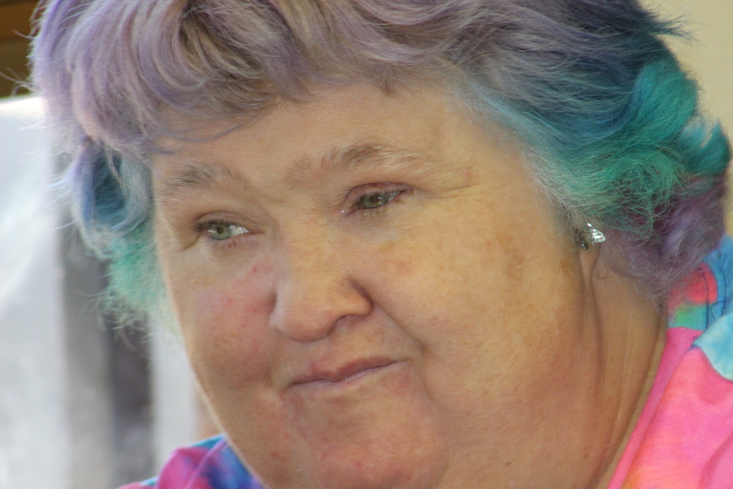 A very close=up, intimate portrait of Sharon, an older lady with multi-colored hair and a very thoughtful look on her face