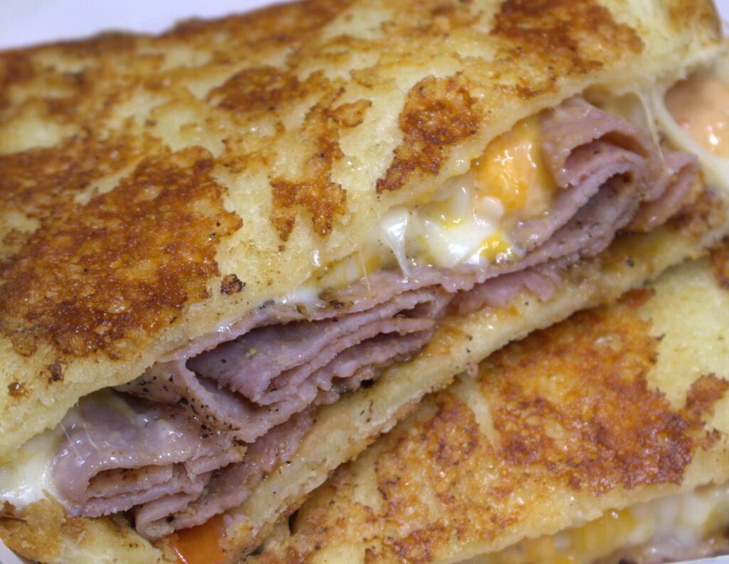 Awesome grilled cheese busting out with beautiful melted cheese and the choicest of ham. Image invokes immediate craving for the best grilled cheese.