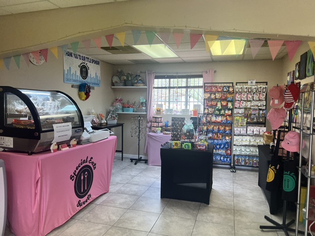 Interior of the Special Eats Sweets store featuring a candy display, refrigerated dessert case, gift items, and colorful decorations in the new location.